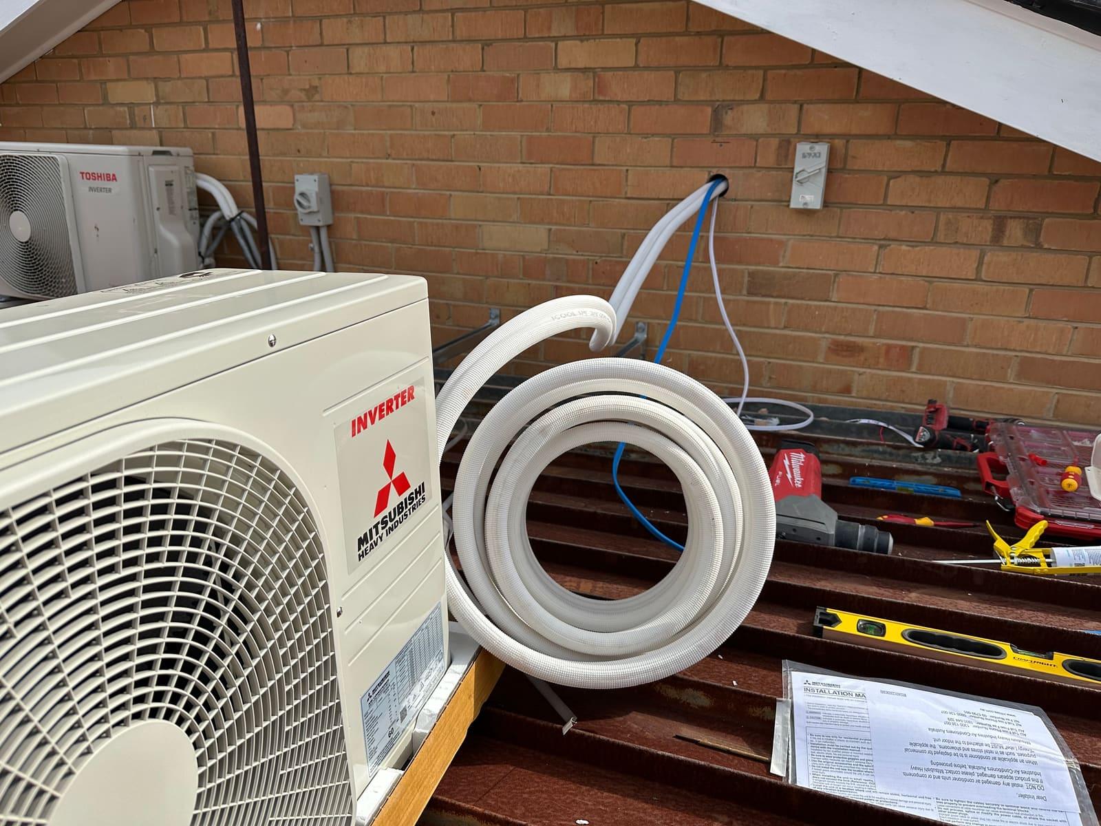 Mitsubishi Heavy Industries inverter outdoor unit during a split system installation, with insulated refrigerant pipework